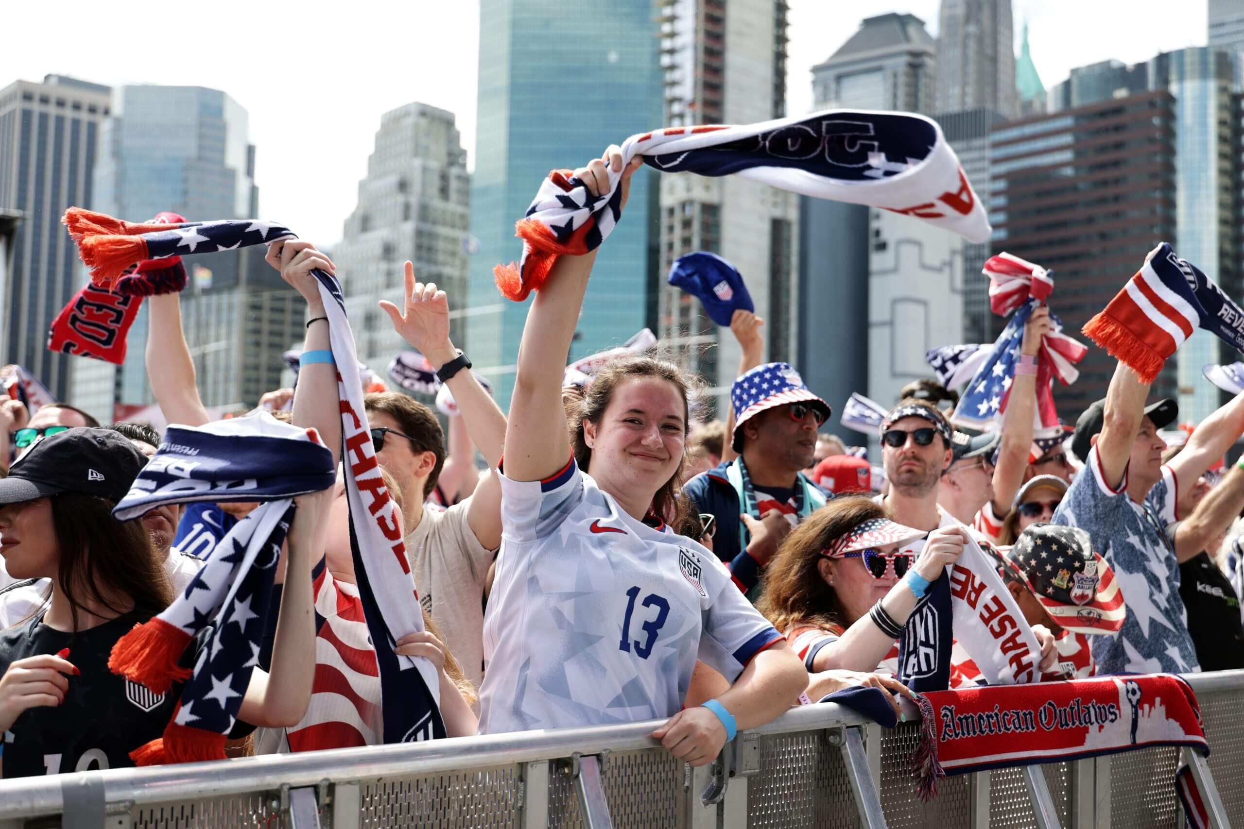 A woman in a United States soccer jersey waves a flag, surrounded by people